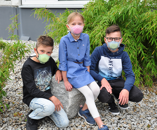 3 Kinder sitzend mit Mund-Nasenschutz-Maske